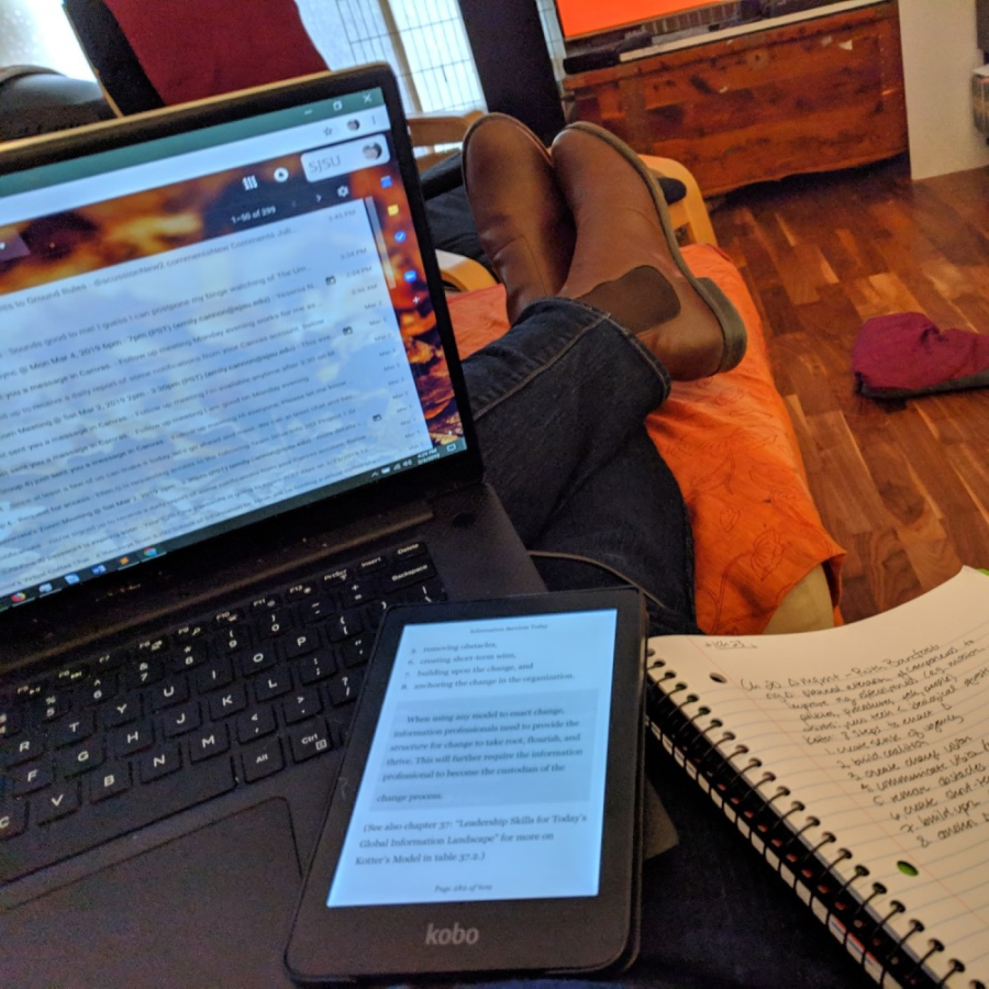 A laptop, an e-reader, a notebook, and feet up on an ottoman